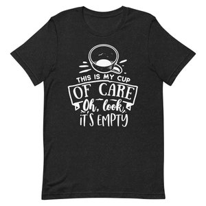 Pode incluir: Uma camiseta preta com um gráfico branco de uma xícara de café e o texto "This is my cup of care. Oh, look, it's empty."