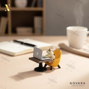May include: A miniature figurine of a cat working on a laptop at a small desk with a yellow chair. A white coffee mug and a notebook are in the background. The figurine is on a light pink surface. The Novara Home Studio logo is in the bottom right corner.