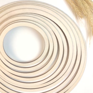 May include: A set of ten concentric wooden hoops, all in a cream colour, arranged in a circular pattern. The hoops are of varying sizes, with the smallest hoop in the centre and the largest hoop on the outside.