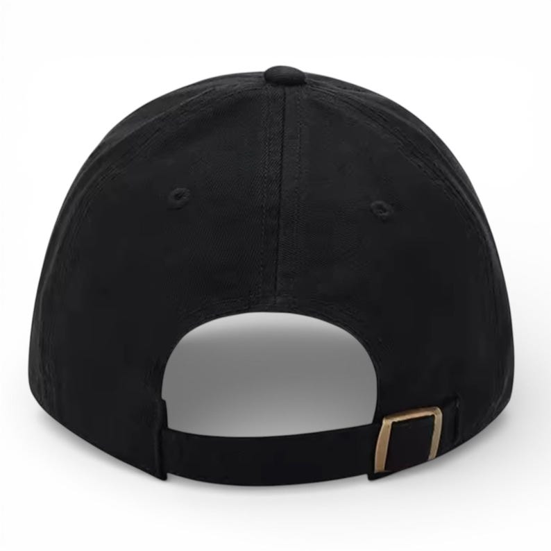 May include: A solid black baseball cap with a curved brim. The back features an adjustable strap with a gold-colored metal buckle. The cap is made of a smooth, matte fabric.