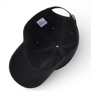 May include: A black baseball cap with a curved brim, a fabric strap, and a metal buckle. The interior of the cap is visible, showing the seams and a small tag. The cap is made of a soft, durable material.