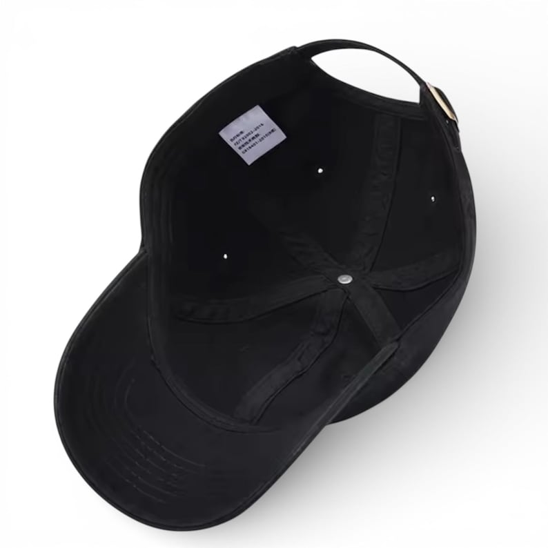 May include: A black baseball cap with a curved brim, a fabric strap, and a metal buckle. The interior of the cap is visible, showing the seams and a small tag. The cap is made of a soft, durable material.