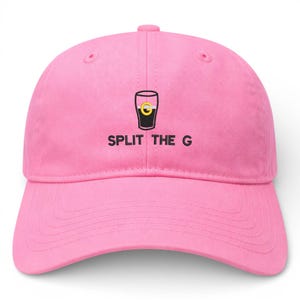 May include: A pink baseball cap with a curved brim. The cap features a graphic of a pint glass with a yellow and black design, and the text "SPLIT THE G" in black letters.
