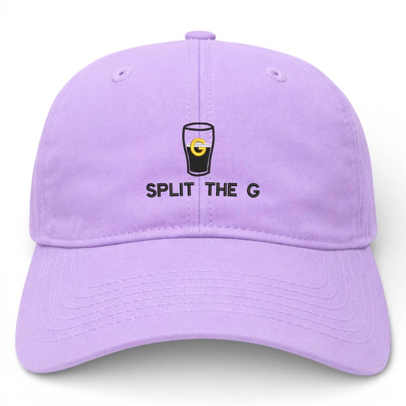 May include: A light purple baseball cap with a curved brim. The cap features a graphic of a black pint glass with a gold "G" inside and the text "SPLIT THE G" in black letters.