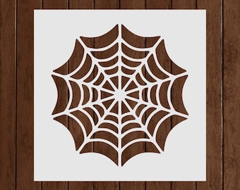 May include: A white stencil featuring a detailed spiderweb design. The web has a circular shape with radiating lines and curved segments, perfect for Halloween or spooky crafts. The stencil is set against a dark wood background.