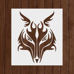 May include: A stencil featuring a stylized wolf head design. The wolf's face is depicted with sharp angles and flame-like details, creating a tribal or abstract aesthetic. The design is in a dark brown color, set against a white background.