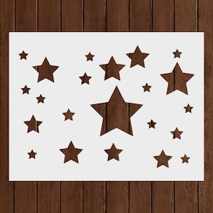 May include: A white stencil featuring a pattern of various-sized stars. The stars are cut out, revealing the brown wooden background. The design includes both large and small stars, creating a celestial theme. Ideal for crafting and decorative projects.