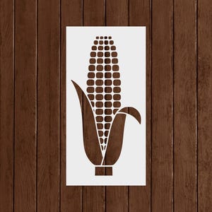 May include: A brown stencil of an ear of corn, featuring a detailed pattern of kernels and leaves. The stencil is rectangular and set against a wooden background, ideal for crafting or home decor projects.