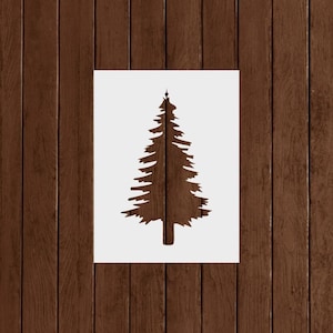 May include: A brown fir tree stencil on a white background. The tree is a silhouette with detailed branches and a pointed top. The background is a wooden surface with vertical planks.