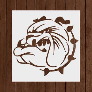 May include: A stencil featuring a detailed illustration of a bulldog's head, showcasing its aggressive expression. The design is in a dark brown color, with sharp lines and a bold outline, perfect for various crafting projects.