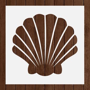 May include: A white seashell stencil design against a dark brown wooden background. The seashell is a detailed outline, with radiating lines and a curved base. The wood grain adds texture and warmth to the design.