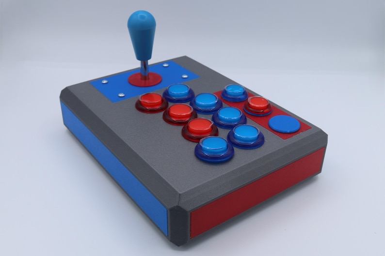 May include: A custom-built arcade joystick with a gray body, red and blue accents, and a blue joystick. It features red and blue buttons arranged in a classic layout, perfect for retro gaming enthusiasts.