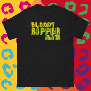 Peut inclure: T-shirt noir avec l'inscription "BLOODY RIPPER MATE" en vert et jaune. Le t-shirt a un col rond et des manches courtes. Le fond présente un motif léopard coloré.