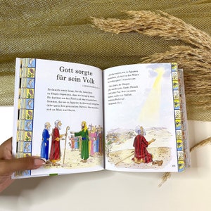 May include: An open book with colorful illustrations depicting a biblical story. The text on the page reads "Gott sorgte fur sein Volk" which translates to "God cared for his people".