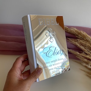 May include: A silver-colored Bible with the word "BIBEL" and a cross design. The name "Elsa" is written in cursive. The text "Vater, vergib ihnen, denn sie wissen nicht, was sie tun [23:34]" is also visible.