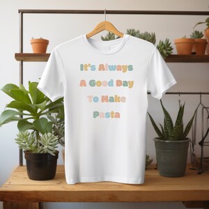 Könnte beinhalten: Weißes T-Shirt mit dem Text "It's Always A Good Day To Make Pasta" in bunten, stilisierten Buchstaben.