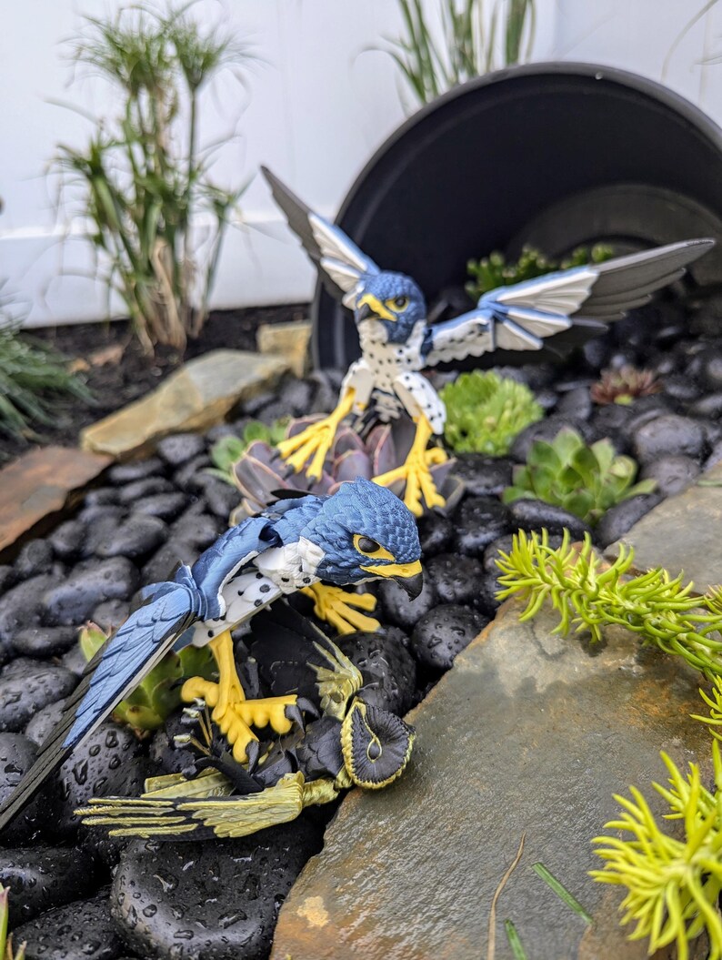 May include: Two blue and white toy falcons with yellow talons are perched on rocks. One falcon is attacking a smaller yellow and black toy falcon.