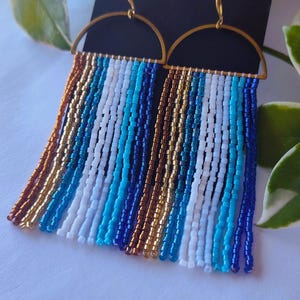 shades of blue with white, gold and bronze beads on raw brass semi-circle