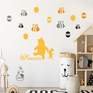 May include: Winnie the Pooh and Piglet wall decals in yellow and gray. The decals feature Winnie the Pooh and Piglet walking together. The decals are surrounded by honey pots and bees. The text "Winston" is written below the characters.