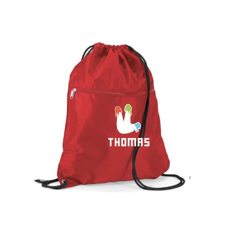 Peut inclure: Un sac &agrave; cordon rouge avec une fermeture &agrave; cordon noire et une poche zipp&eacute;e. Le sac pr&eacute;sente un motif blanc de gouttes de peinture vertes, jaunes et bleues, avec le nom "THOMAS" imprim&eacute; en dessous en lettres blanches.