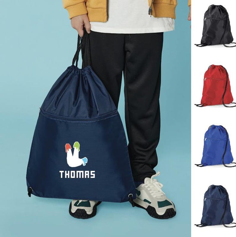 Peut inclure: Un sac &agrave; dos de sport bleu marine avec un motif blanc et le nom "THOMAS" imprim&eacute; en blanc. Le motif pr&eacute;sente une forme blanche avec des &eacute;claboussures de peinture rouge, verte et bleue. Le sac &agrave; dos a une poche zipp&eacute;e et des cordons noirs.