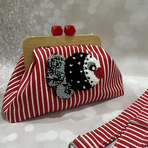 以下が含まれることがあります： 木製のフレームと赤い幾何学的な留め金が付いた、赤と白のストライプのクラッチバッグ。クラッチバッグは、黒、白、赤の装飾的なアップリケが特徴です。シルバーの金具が付いたお揃いの赤と白のストライプのストラップも含まれています。
