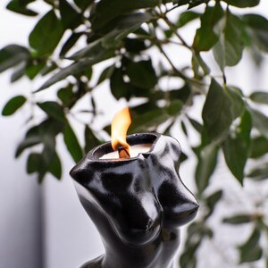 May include: A black candle shaped like a human torso with a flame burning at the top.