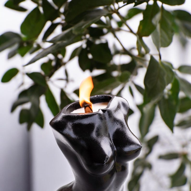 May include: A black candle shaped like a human torso with a flame burning at the top.