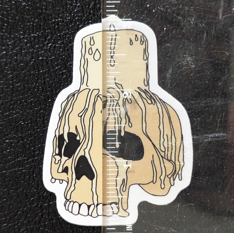 May include: A sticker of a skull with dripping wax, resembling a candle. The skull is beige with black eye sockets and a white background.
