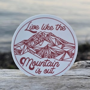May include: A white round sticker with a red geometric mountain design and the text "Live like the mountain is out".
