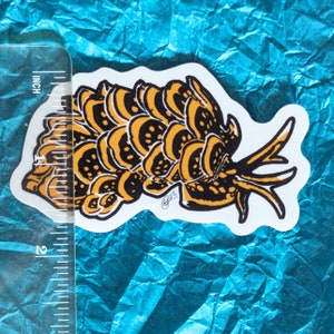 May include: A black and yellow sticker of a sea slug with a textured, segmented body. The sticker is on a blue background.