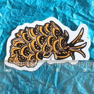 May include: A black and yellow sticker of a stylized sea slug with a textured, segmented body. The sticker is approximately 2 inches long.