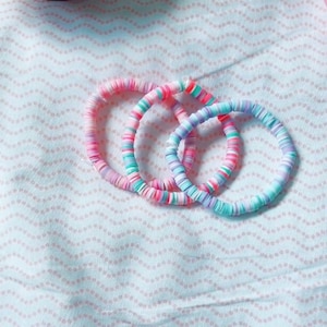 May include: Three colorful bracelets made of stacked, round, plastic beads. The bracelets are pink, blue, and green.