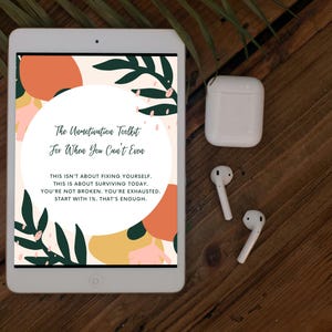 May include: A white tablet displays a colorful graphic with text: "The Unmotivation Toolkit For When You Can't Even." White wireless earbuds and a charging case sit on a wooden surface. The tablet's screen features abstract shapes and botanical elements.