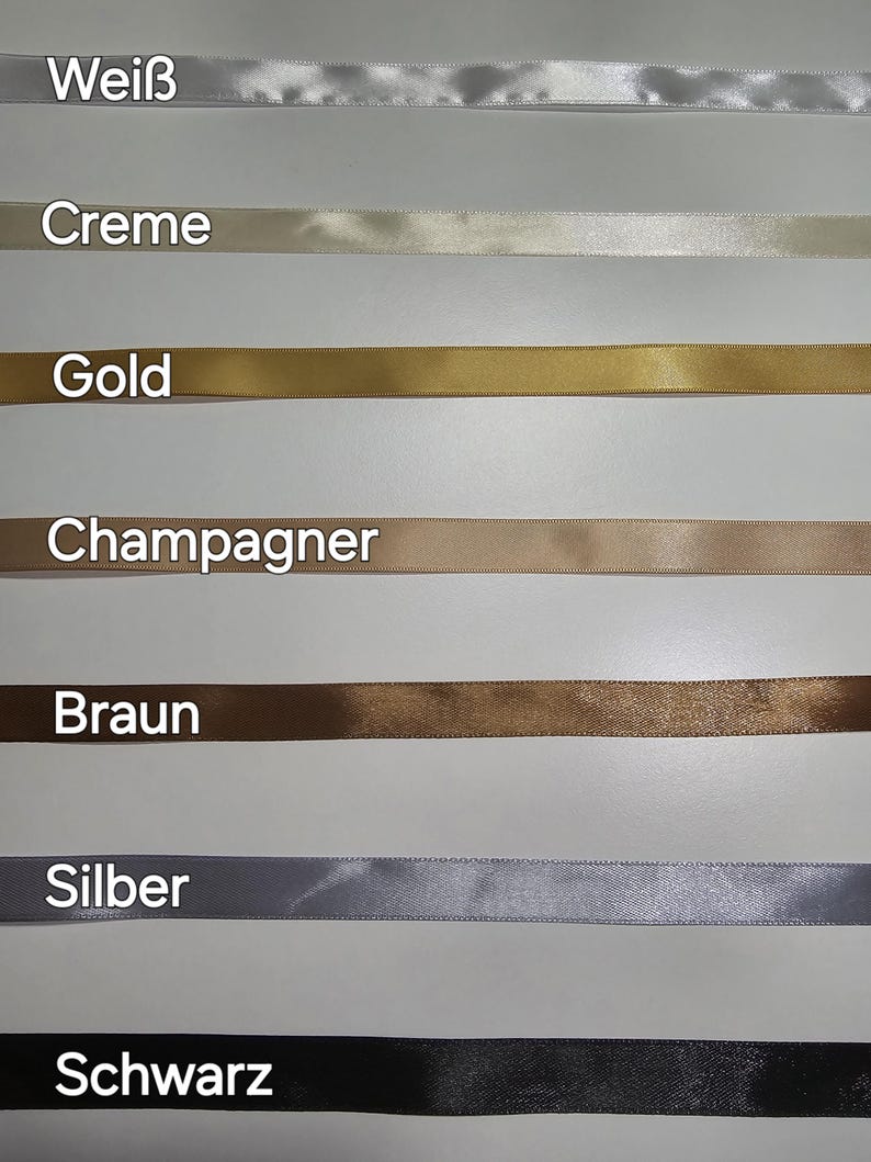 Pu&ograve; includere: Una selezione di nastri di raso in vari colori, tra cui bianco, crema, oro, champagne, marrone, argento e nero. Ogni nastro &egrave; etichettato con il suo nome di colore in tedesco. I nastri sono disposti orizzontalmente.
