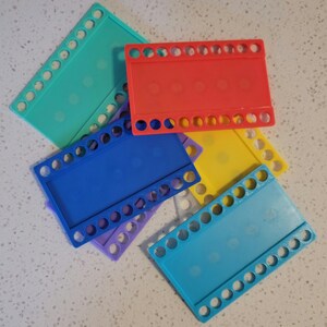 May include: Five plastic loom boards in different colors: turquoise, red, yellow, blue, and light blue. Each board has a rectangular shape with rows of holes around the edges.