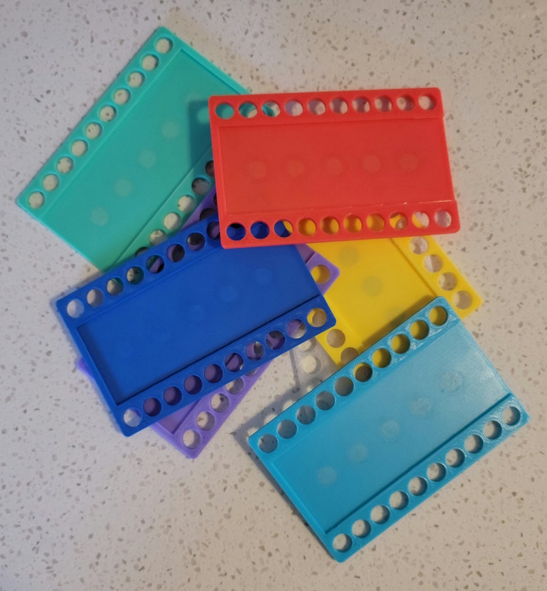 May include: Five plastic loom boards in different colors: turquoise, red, yellow, blue, and light blue. Each board has a rectangular shape with rows of holes around the edges.
