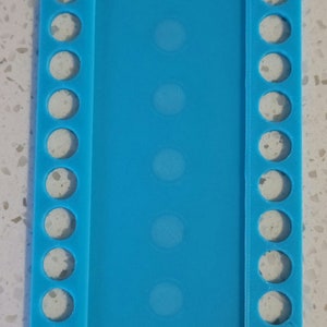May include: A light blue plastic embroidery floss organizer with 10 rows of holes on each side and 5 rows of holes in the center.