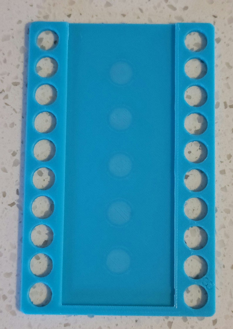 May include: A light blue plastic embroidery floss organizer with 10 rows of holes on each side and 5 rows of holes in the center.