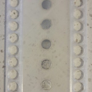 May include: A white plastic tray with 10 round holes and 5 silver metal discs with a textured surface.