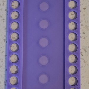 May include: Purple plastic thread organizer with 10 round holes on each side and 5 clear rectangular slots in the center.