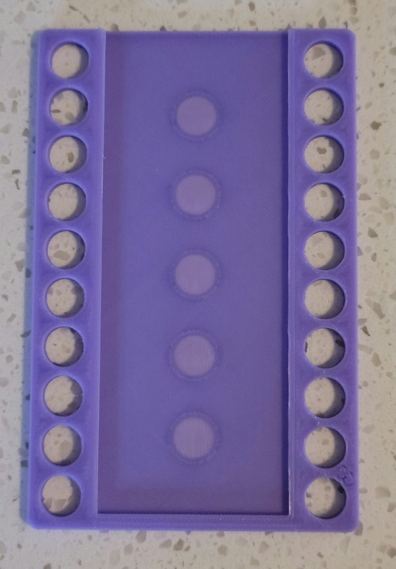 May include: Purple plastic thread organizer with 10 round holes on each side and 5 clear rectangular slots in the center.