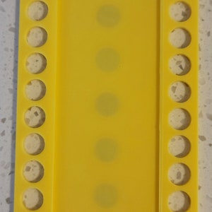 May include: A yellow plastic bead organizer with rows of holes for storing beads. The organizer has a clear plastic panel in the center.