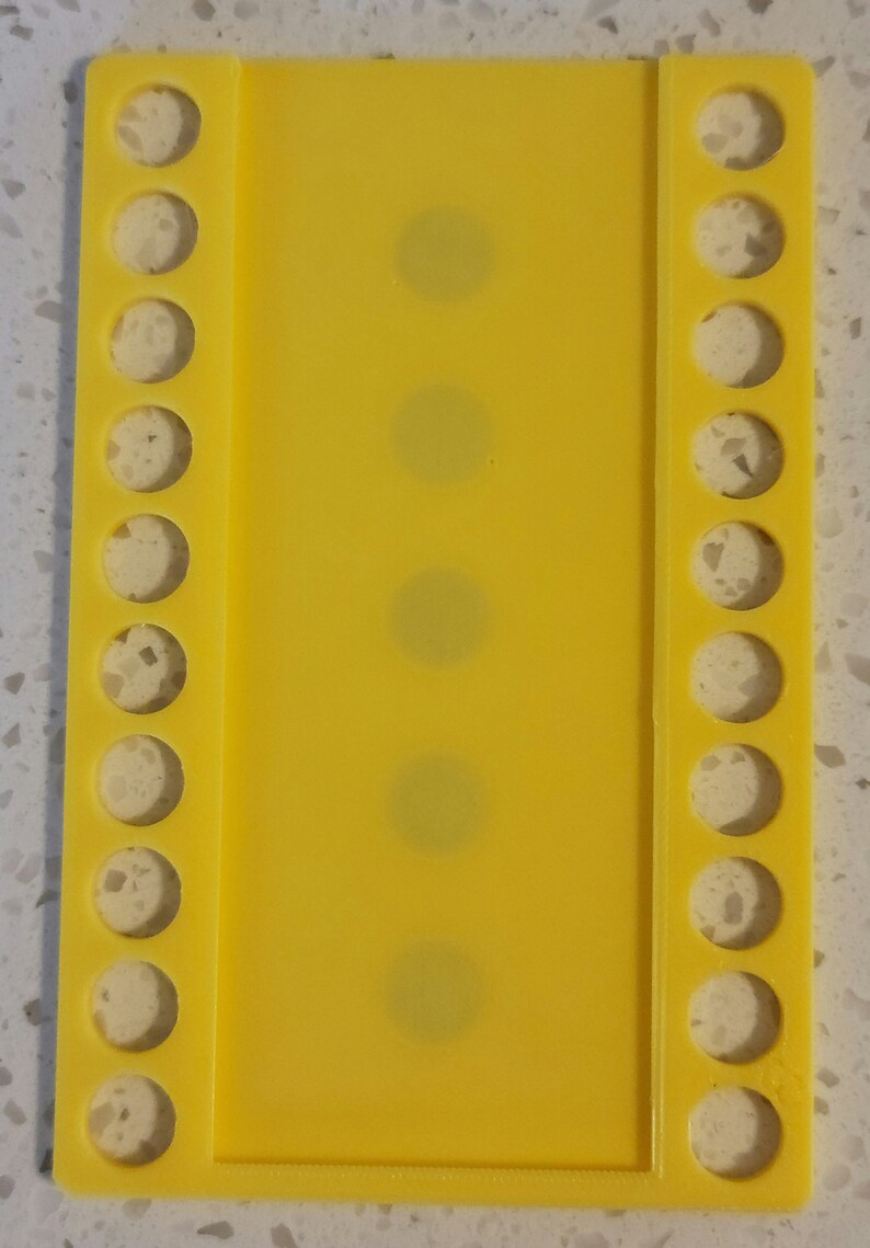 May include: A yellow plastic bead organizer with rows of holes for storing beads. The organizer has a clear plastic panel in the center.