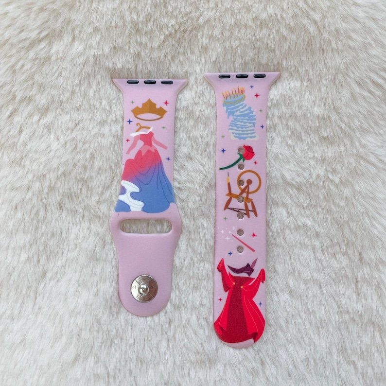 May include: Pink Apple Watch band with a Sleeping Beauty design. The band features a pink background with illustrations of Sleeping Beauty, a spinning wheel, a rose, and a crown.