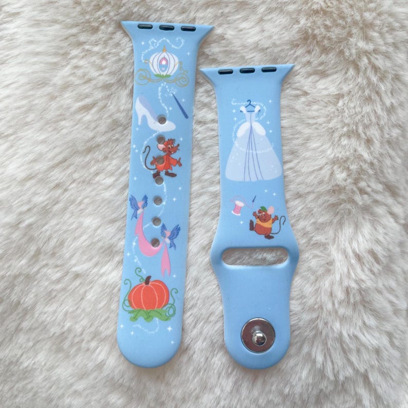 May include: Two light blue watch bands with a fairytale theme. One band features a pumpkin, carriage, glass slipper, and mice. The other band has a dress, spool of thread, and a mouse. The bands are made of a flexible material.