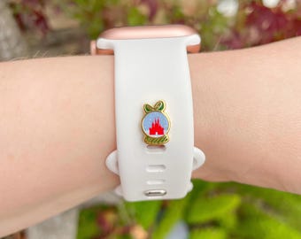 Puede incluir: Correa blanca para Apple Watch con caja dorada. La correa presenta un dije de esmalte colorido con un diseño de castillo. El dije tiene detalles en rojo, azul y verde. El reloj está en una muñeca.