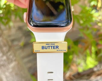May include: A gold-colored watch band with a gold-colored metal band that says "SWEET CREAM BUTTER GRADE AA NET WT. 4OZ (113 g)".