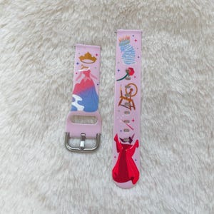 May include: A pink silicone watch band with a colorful design featuring a princess, a crown, a spinning wheel, and a rose. The band is designed for a smartwatch.