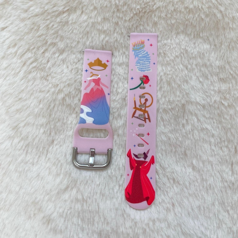 May include: A pink silicone watch band with a colorful design featuring a princess, a crown, a spinning wheel, and a rose. The band is designed for a smartwatch.